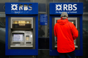 A pedestrian uses a automated teller machine (ATM) outside a closed Royal Bank of Scotland Group Plc bank branch in Hove, near Brighton, U.K., on Wednesday, Jan. 27, 2016. RBS said it will take a 3.6 billion-pound ($5.2 billion) hit to the value of its assets and set aside more money for past misconduct, overshadowing Chief Executive Officer Ross McEwan's efforts to resume dividend payments next year. Photographer: Luke MacGregor/Bloomberg via Getty Images